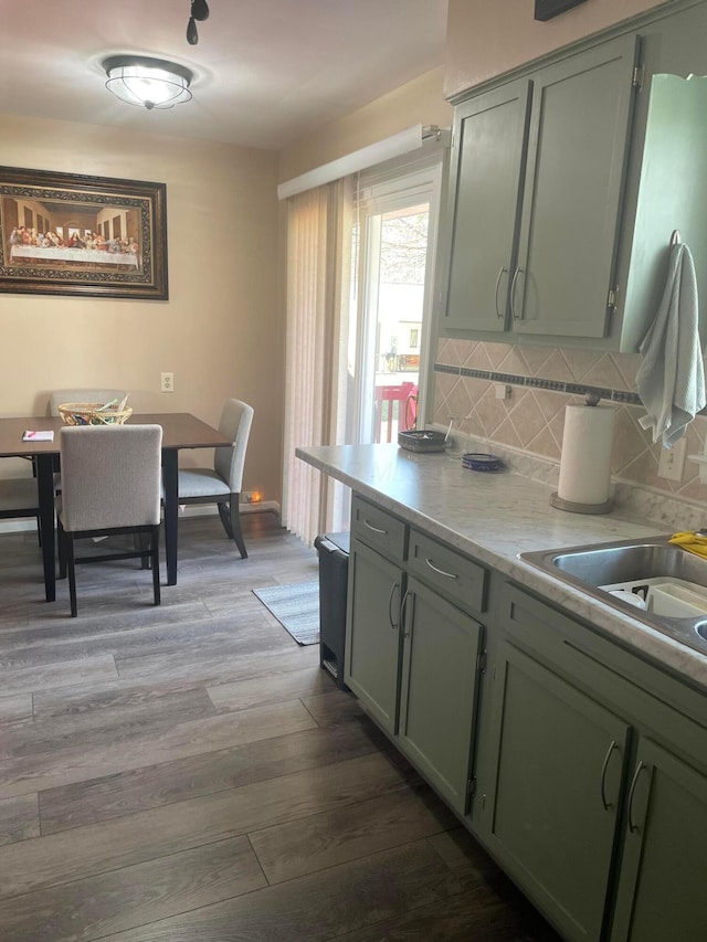 kitchen featuring light wood finished floors, a sink, light countertops, green cabinets, and backsplash