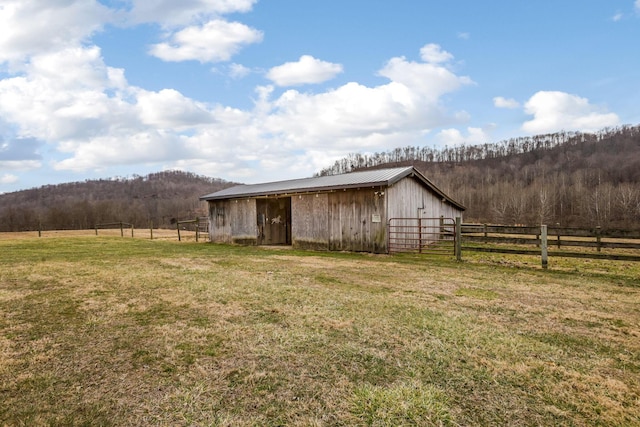 view of outdoor structure featuring a rural view, a wooded view, an outdoor structure, and fence