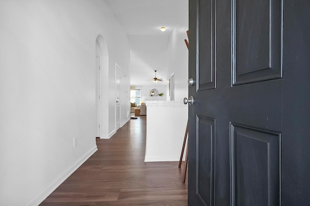 hallway featuring baseboards, arched walkways, and dark wood finished floors