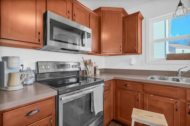 kitchen featuring a sink, appliances with stainless steel finishes, brown cabinetry, and hanging light fixtures