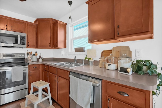 kitchen with pendant lighting, a sink, wood finished floors, stainless steel appliances, and brown cabinetry