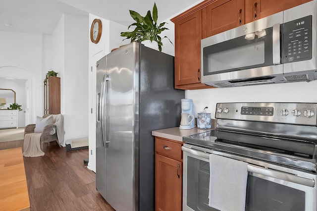 kitchen featuring brown cabinetry, appliances with stainless steel finishes, and dark wood-style flooring