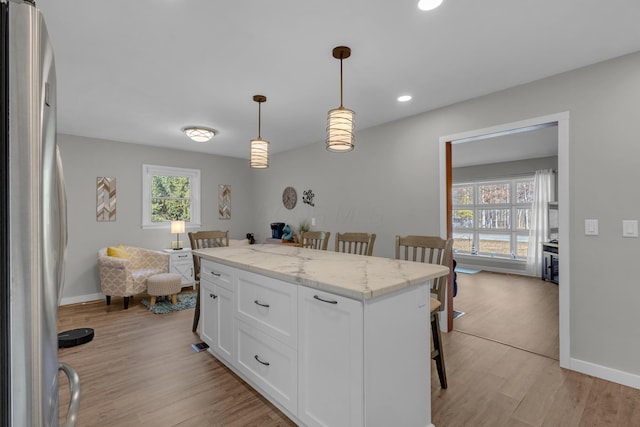 kitchen with freestanding refrigerator, white cabinets, pendant lighting, a kitchen breakfast bar, and light wood-type flooring