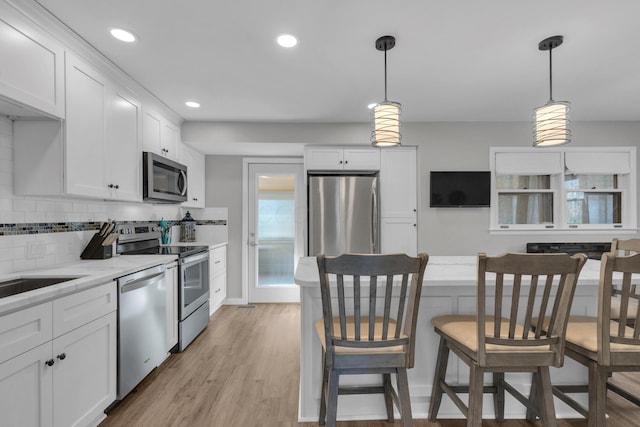 kitchen with decorative light fixtures, white cabinetry, appliances with stainless steel finishes, light wood finished floors, and decorative backsplash