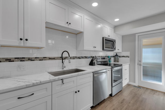 kitchen featuring light wood finished floors, light stone countertops, white cabinets, stainless steel appliances, and a sink