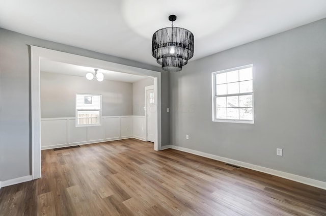 unfurnished dining area featuring an inviting chandelier, wood finished floors, and a healthy amount of sunlight