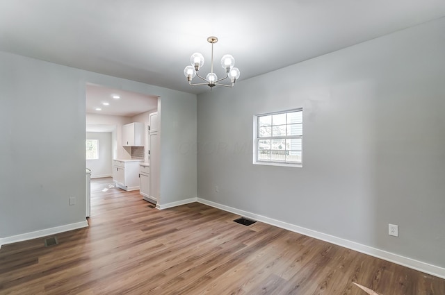 unfurnished dining area with visible vents, light wood-style flooring, recessed lighting, an inviting chandelier, and baseboards