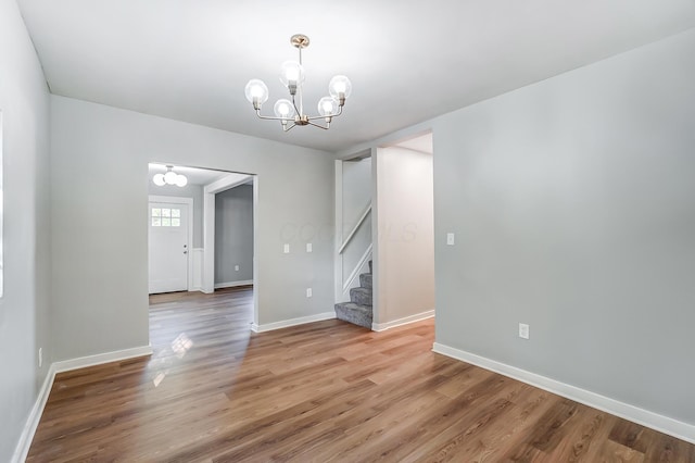 spare room featuring baseboards, an inviting chandelier, stairs, and light wood finished floors