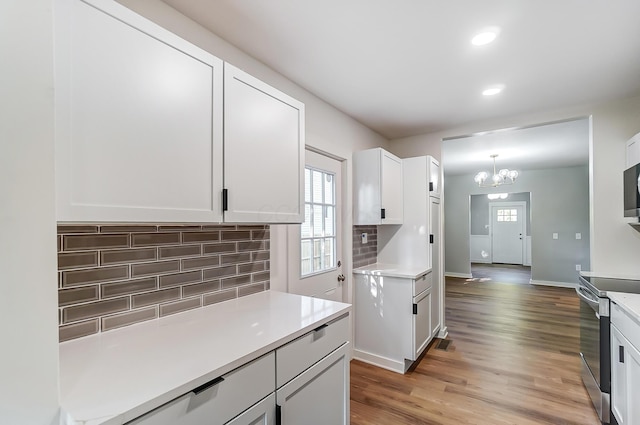 kitchen featuring electric stove, tasteful backsplash, white cabinetry, light wood-style floors, and light countertops