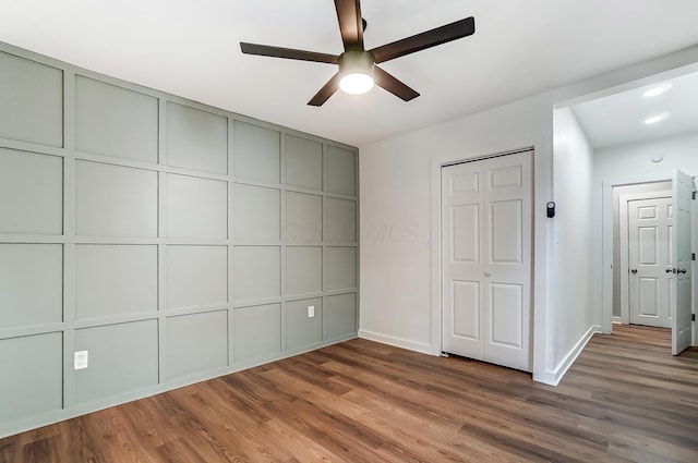 unfurnished bedroom with a ceiling fan, a decorative wall, wood finished floors, and baseboards