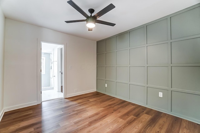 interior space with a decorative wall, baseboards, ceiling fan, and wood finished floors