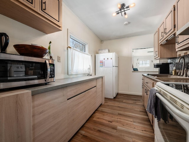 kitchen with white appliances, wood finished floors, baseboards, a sink, and backsplash