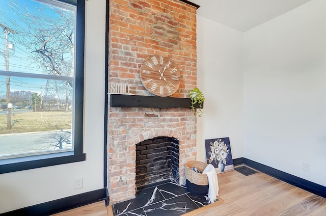 room details featuring visible vents, baseboards, a brick fireplace, and wood finished floors