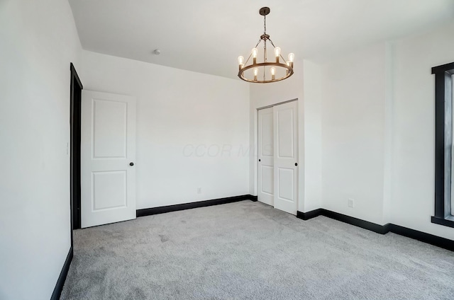 empty room with a notable chandelier, baseboards, and carpet