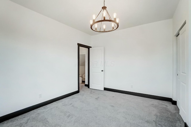 carpeted empty room featuring an inviting chandelier and baseboards