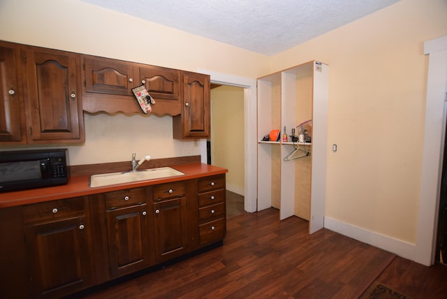 kitchen with black microwave, dark wood finished floors, dark brown cabinetry, a textured ceiling, and a sink