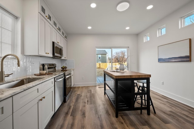 kitchen with a sink, backsplash, white cabinetry, stainless steel appliances, and glass insert cabinets