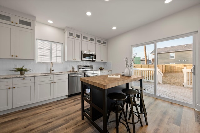 kitchen with tasteful backsplash, butcher block countertops, wood finished floors, stainless steel appliances, and a sink