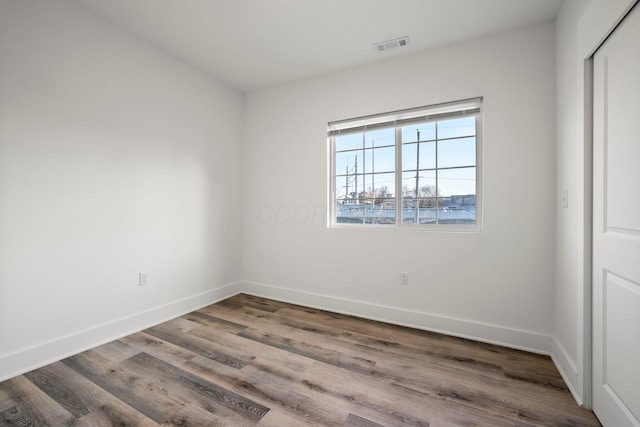 spare room with wood finished floors, visible vents, and baseboards