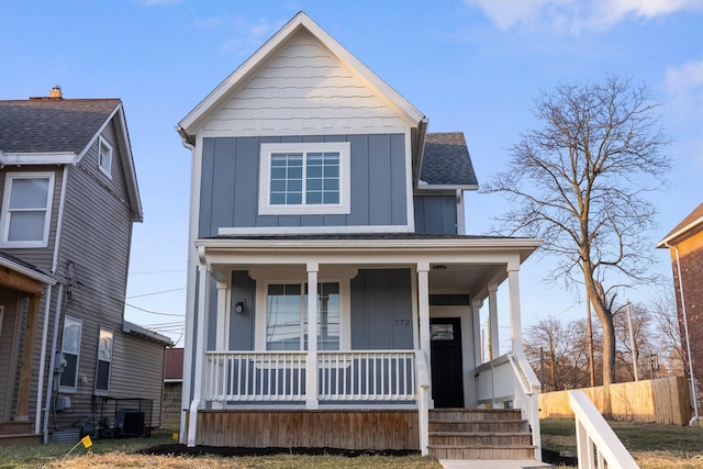 view of front of property with covered porch, board and batten siding, roof with shingles, and fence