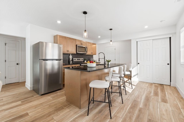 kitchen featuring dark countertops, light wood finished floors, appliances with stainless steel finishes, and a kitchen breakfast bar