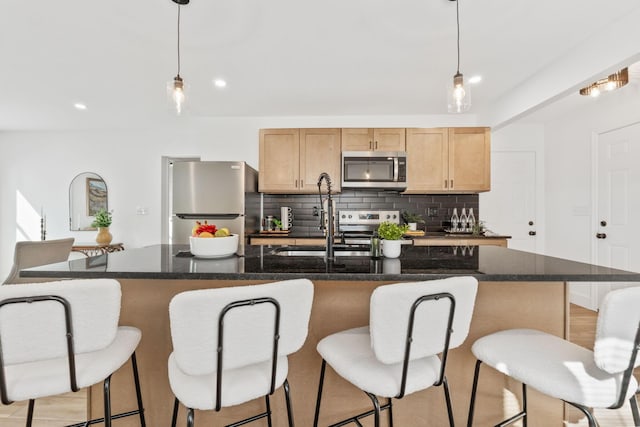 kitchen with tasteful backsplash, decorative light fixtures, a center island with sink, appliances with stainless steel finishes, and a sink