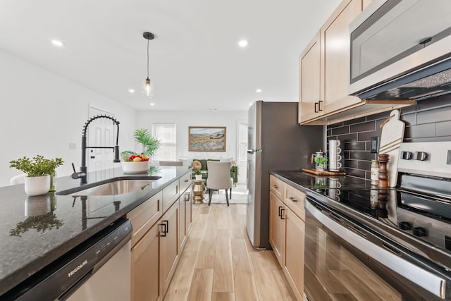 kitchen with light wood-type flooring, a sink, dark stone countertops, tasteful backsplash, and stainless steel appliances