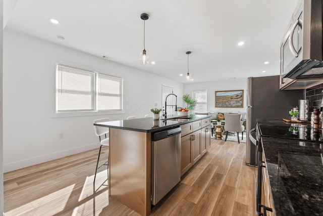 kitchen featuring dark stone countertops, a sink, light wood-style floors, appliances with stainless steel finishes, and a kitchen bar