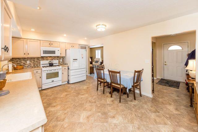 kitchen featuring tasteful backsplash, baseboards, light countertops, white appliances, and a sink