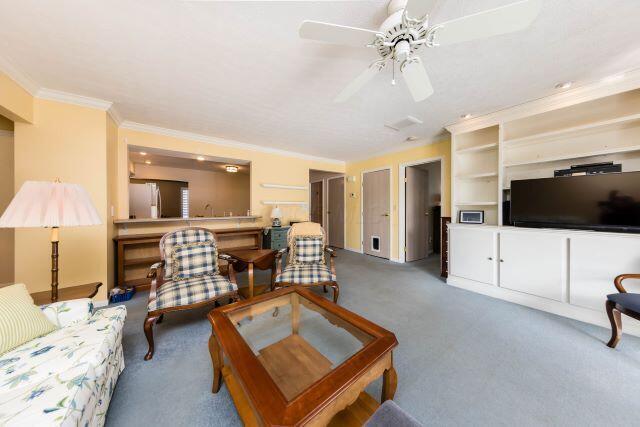 carpeted living area featuring ceiling fan and crown molding