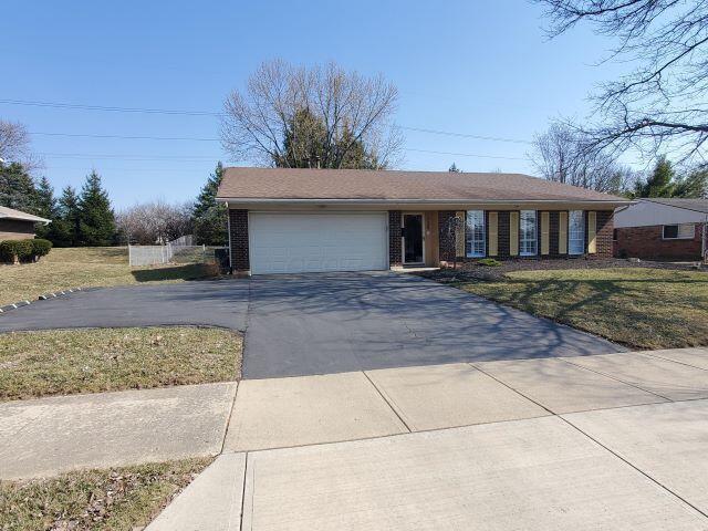 ranch-style home with driveway, brick siding, an attached garage, and a front yard