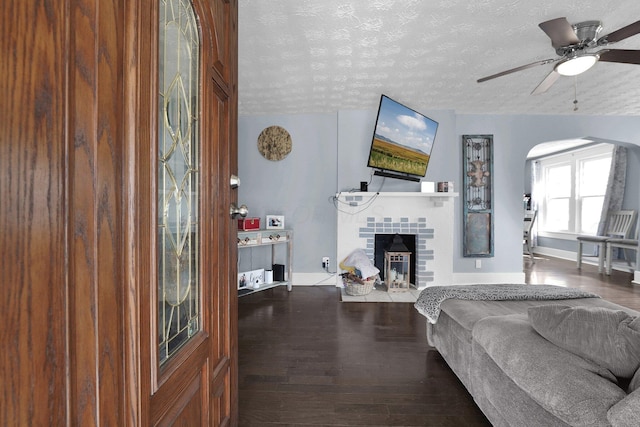 living room featuring a fireplace, a textured ceiling, a ceiling fan, and wood finished floors