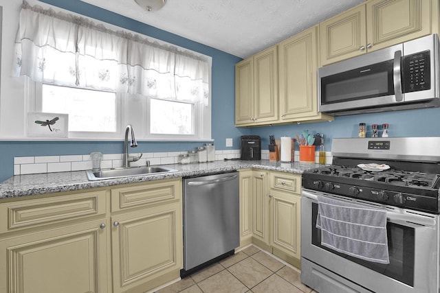 kitchen with cream cabinetry, a sink, a textured ceiling, appliances with stainless steel finishes, and light tile patterned floors