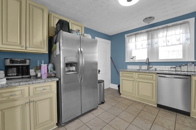 kitchen with light stone countertops, a sink, stainless steel appliances, a textured ceiling, and cream cabinets