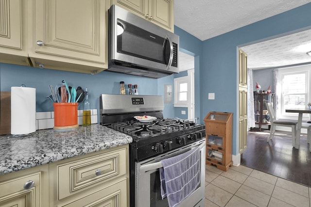 kitchen with light stone countertops, light tile patterned floors, stainless steel appliances, cream cabinetry, and a textured ceiling