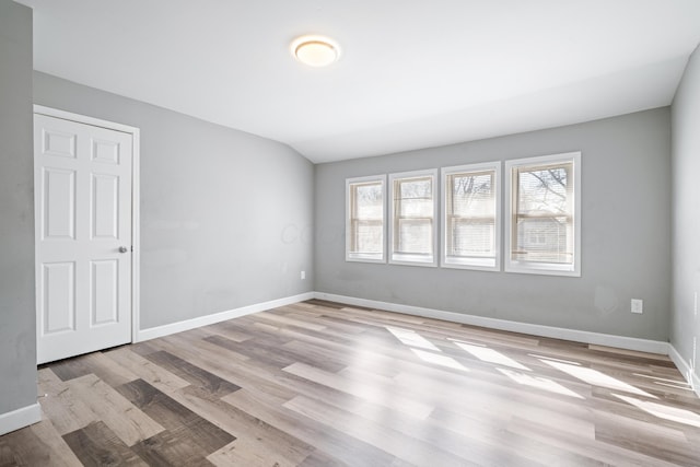 empty room with lofted ceiling, light wood-type flooring, and baseboards