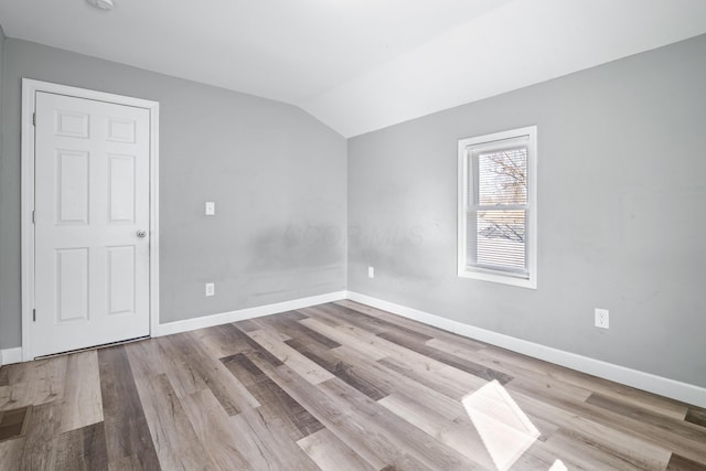 spare room featuring baseboards, lofted ceiling, and wood finished floors