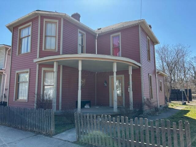 view of front of property with a fenced front yard, a porch, and a chimney