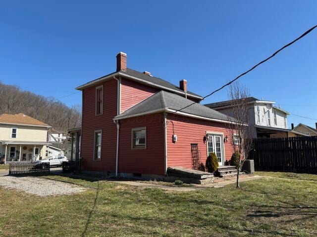 back of property with fence, a lawn, and a chimney