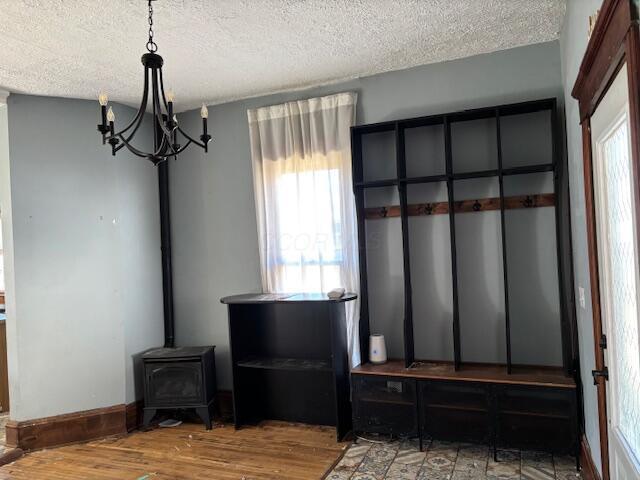 mudroom featuring a notable chandelier, a textured ceiling, wood finished floors, baseboards, and a wood stove