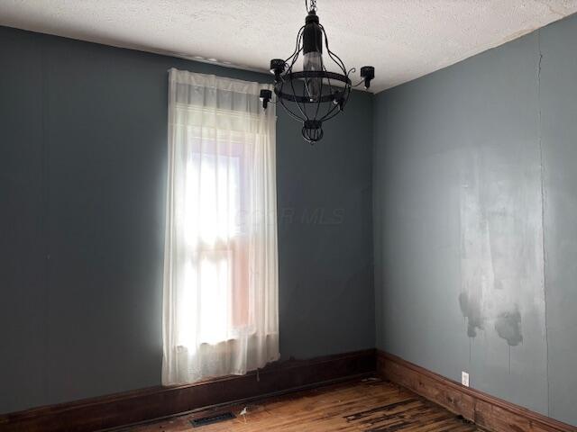 unfurnished room with plenty of natural light, a textured ceiling, an inviting chandelier, and wood finished floors