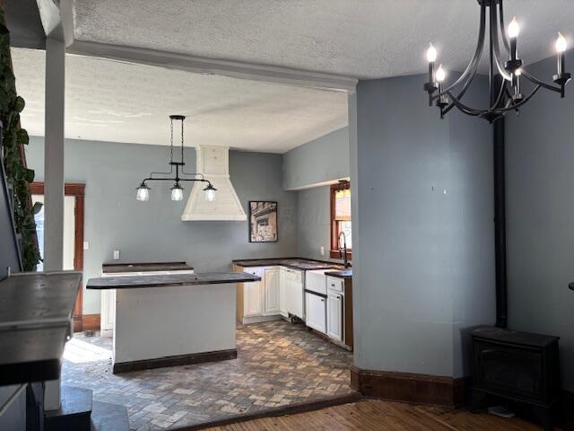 kitchen with dark countertops, a textured ceiling, white cabinets, custom exhaust hood, and a wood stove