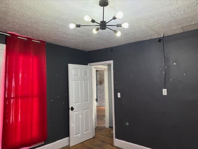 unfurnished bedroom featuring a notable chandelier, baseboards, a textured ceiling, and wood finished floors