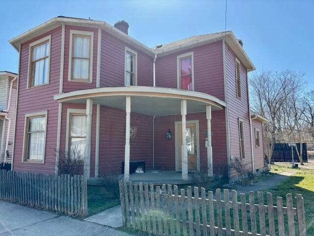 view of front of home featuring covered porch, a fenced front yard, and a chimney