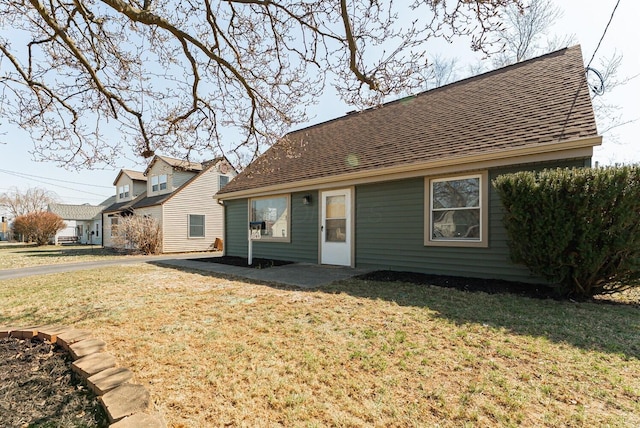 back of property with a patio area, a shingled roof, and a yard