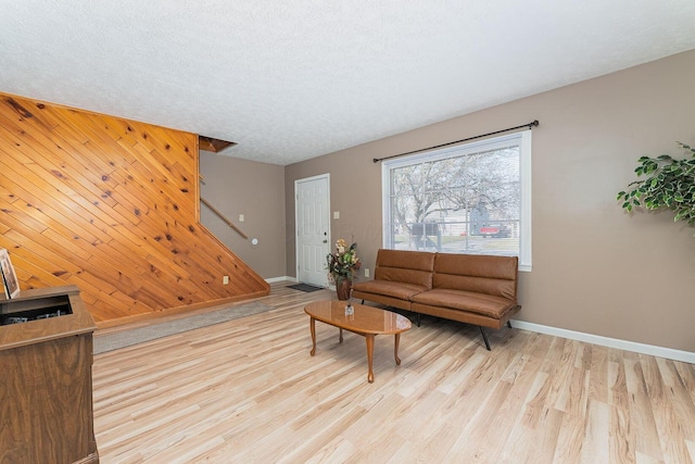 living area featuring a textured ceiling, wood finished floors, stairway, wooden walls, and an accent wall