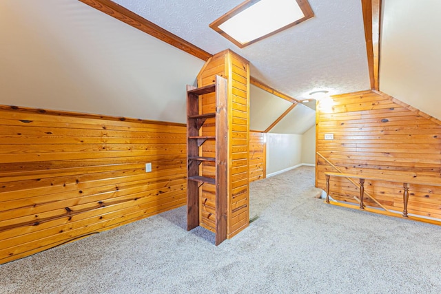 bonus room featuring wooden walls, vaulted ceiling with skylight, a textured ceiling, and carpet