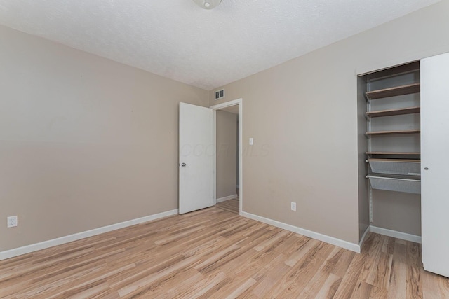 unfurnished bedroom featuring baseboards, visible vents, light wood-type flooring, and a textured ceiling