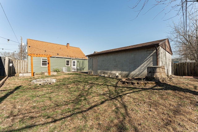 back of house featuring a fenced backyard, a yard, a fire pit, an outdoor structure, and concrete block siding