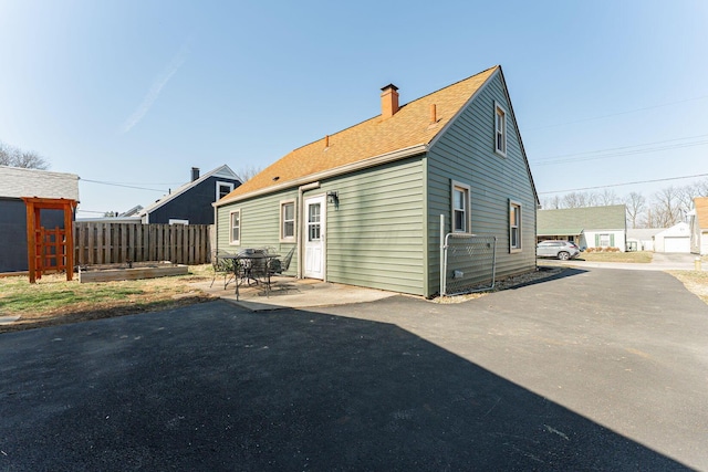 back of property featuring a shingled roof, a patio area, fence, and a chimney